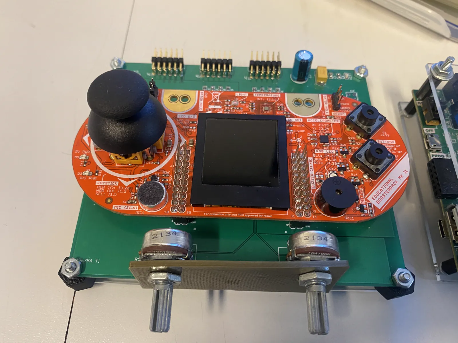 Educational carrier board carrying a sensor pack with joystick, LCD, buttons, buzzer and microphone, plus two potentiometers on a 3D-printed bracket